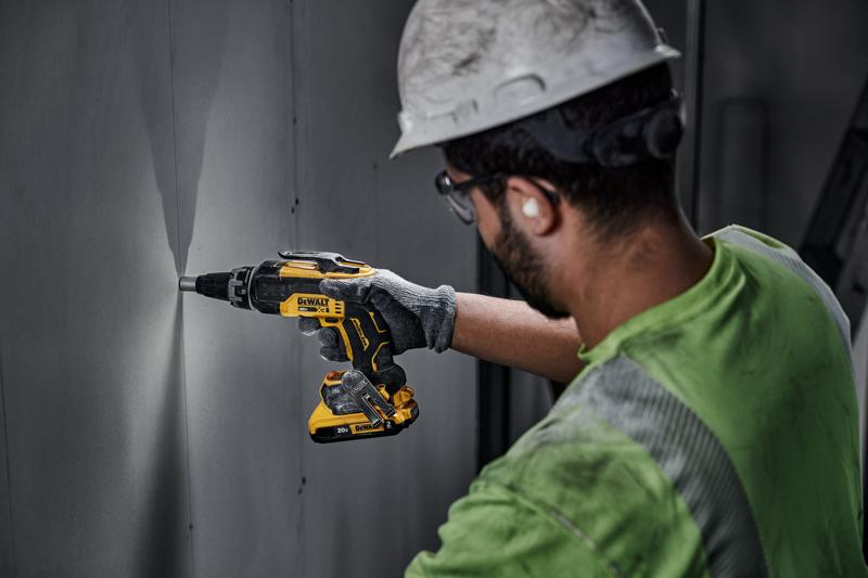 Una persona con casco y guantes utiliza un destornillador inalámbrico DEWALT DCF630D2 para trabajar en un panel de pared en interiores.
